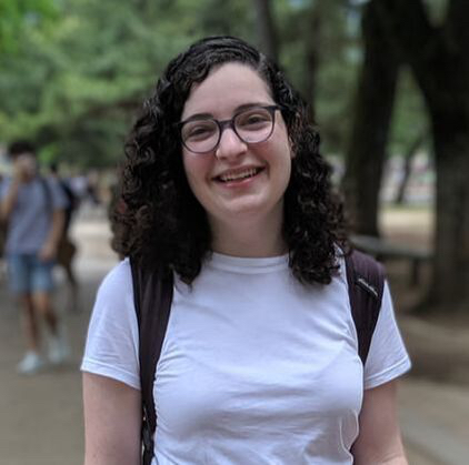 Rebecca Tarnopol smiling to the camera in front of a blurred park background with a purple backpack.